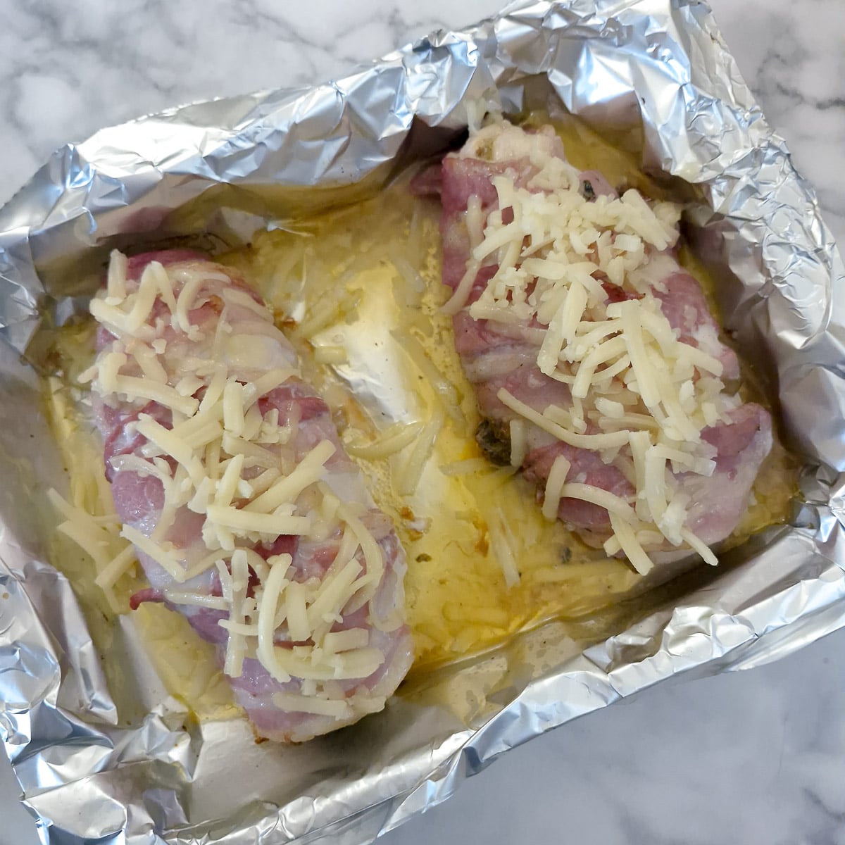 Step 9, grated cheese sprinkled on top of 2 partly cooked bacon-wrapped chicken breasts.