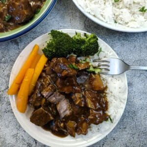 A helping of caramelised pork and pineapple on a bed of white rice on a white plate with carrots and broccoli.