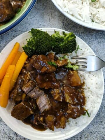 A helping of caramelised pork and pineapple on a bed of white rice on a white plate with carrots and broccoli.