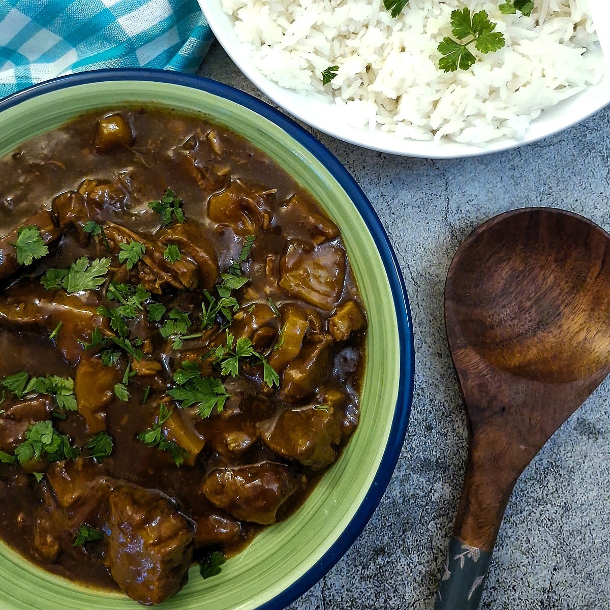 A green serving dish filled with caramelised pineapple pork.
There is a wooden serving spoon on the table and a dish of rice in the background.