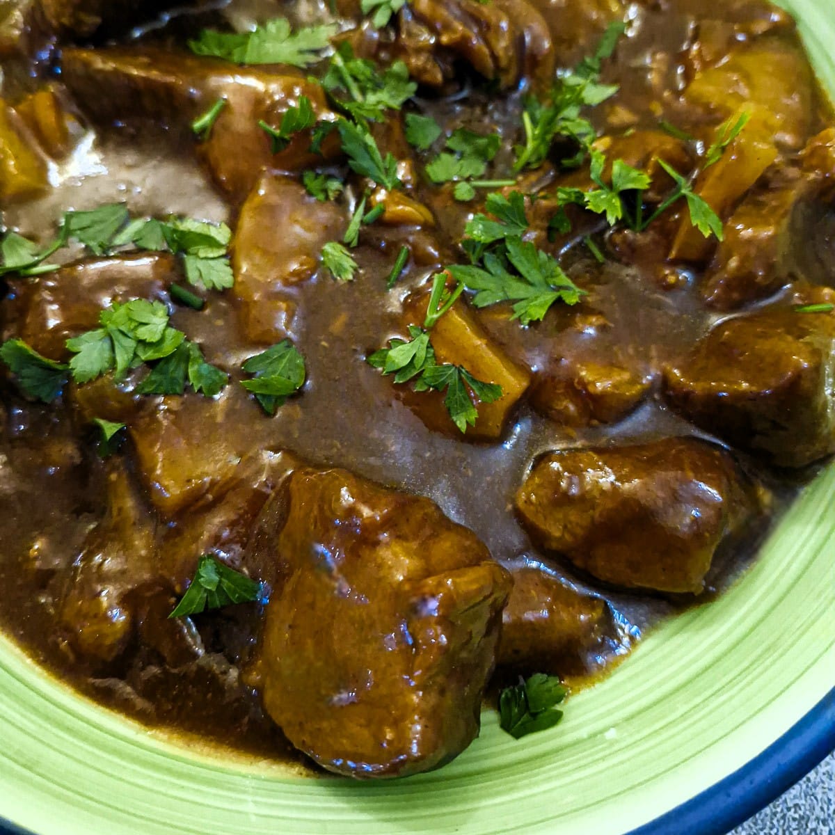 Close up of pineapple pork with lots of gravy in a green dish.