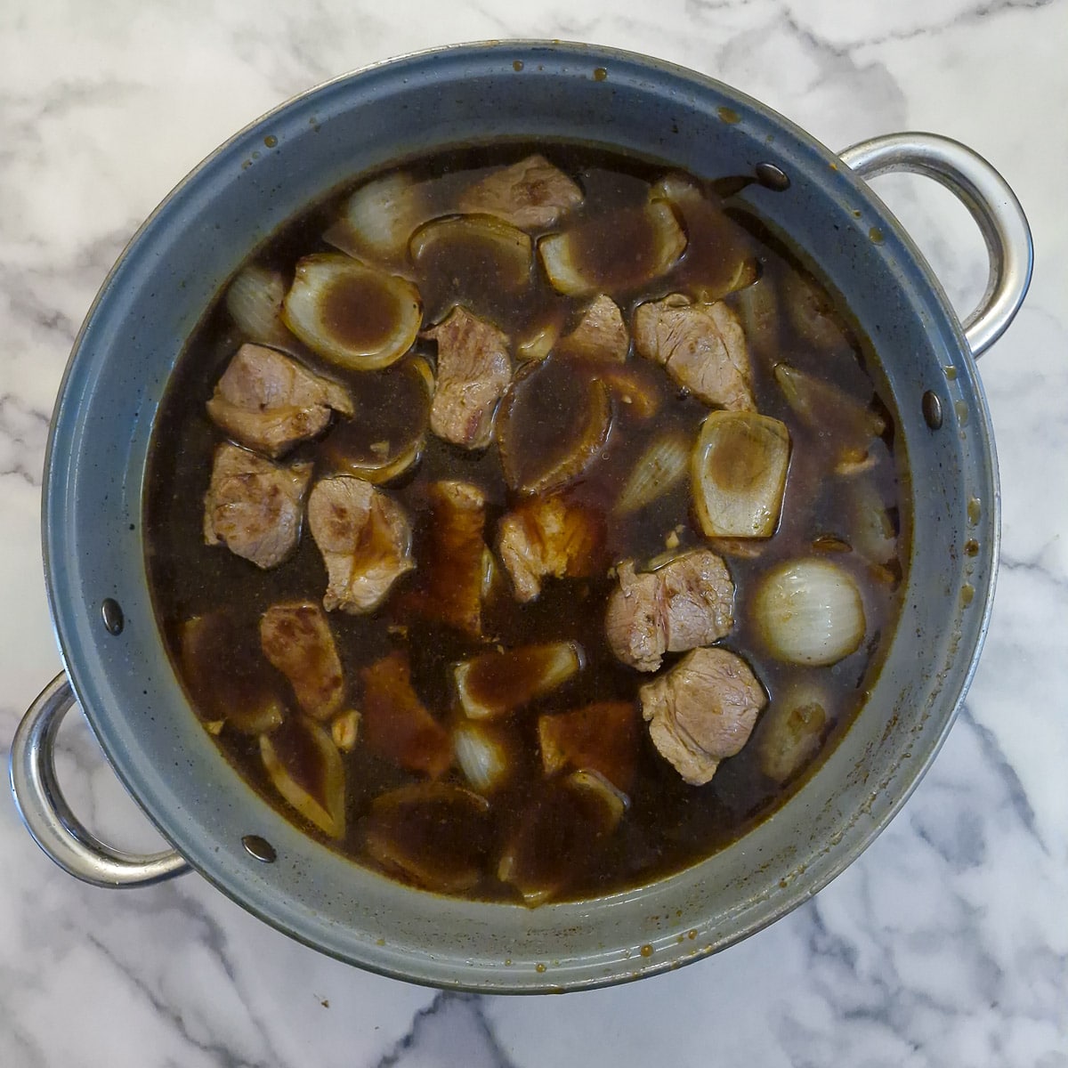 Sauce ingredients and browned pork added to the onions in a large pan.