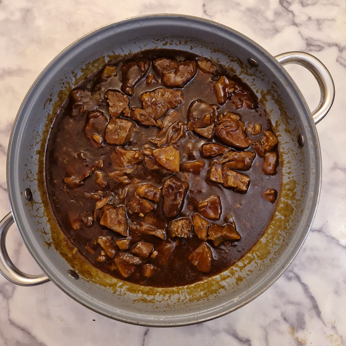 A pan of fully cooked pineapple pork and onions with lots of sauce.