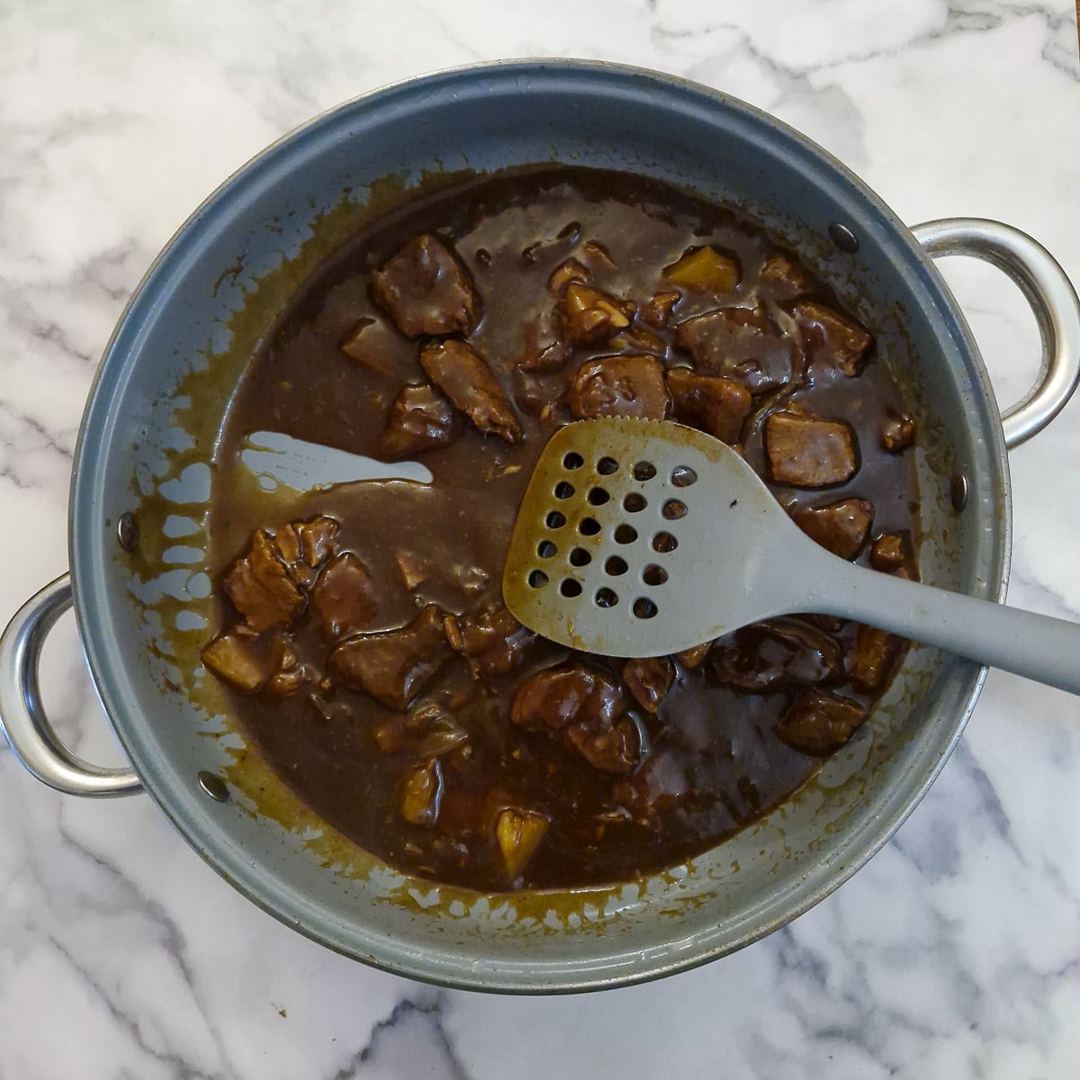 A spatula being drawn through the pork, showing the consistency of the sauce.