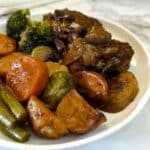 A dinner plate with 2 patties of Salisbury steak smothered with mushroom and onion gravy, with a selection of potatoes and vegtables on the side.