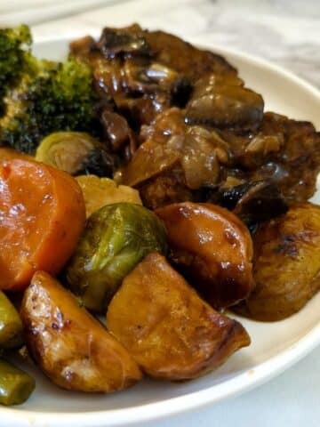 A dinner plate with 2 patties of Salisbury steak smothered with mushroom and onion gravy, with a selection of potatoes and vegtables on the side.
