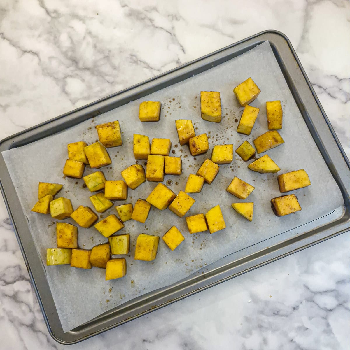 Cubed, coated buternut arranged on a baking tray.