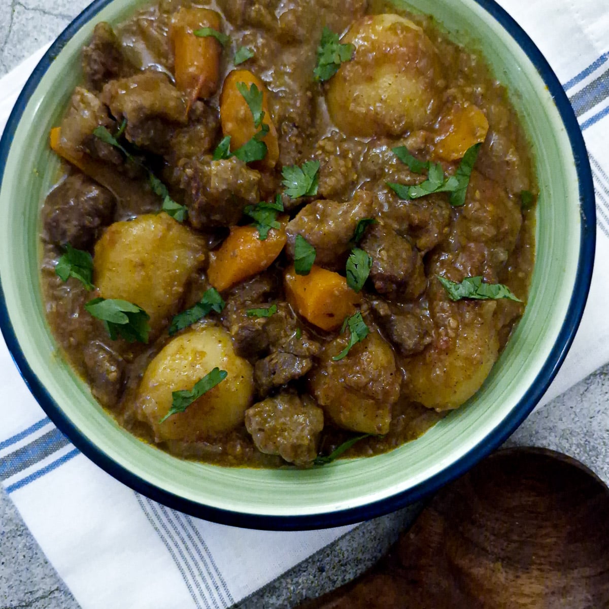 Overhead shot of a dish of lamb bredit on a blue and white checked cloth.
