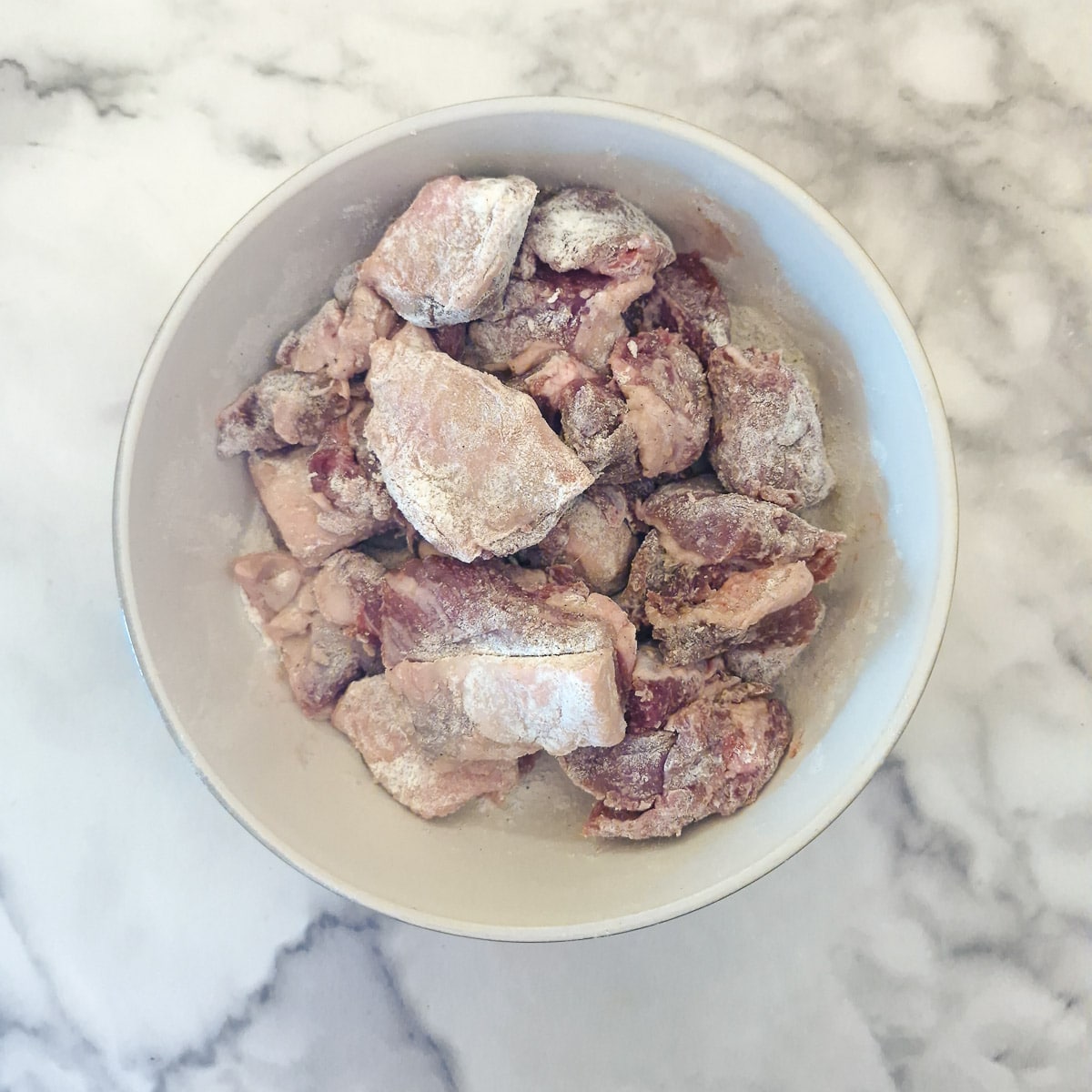 Step 1, Lamb pieces coated in flour in a small white bowl.