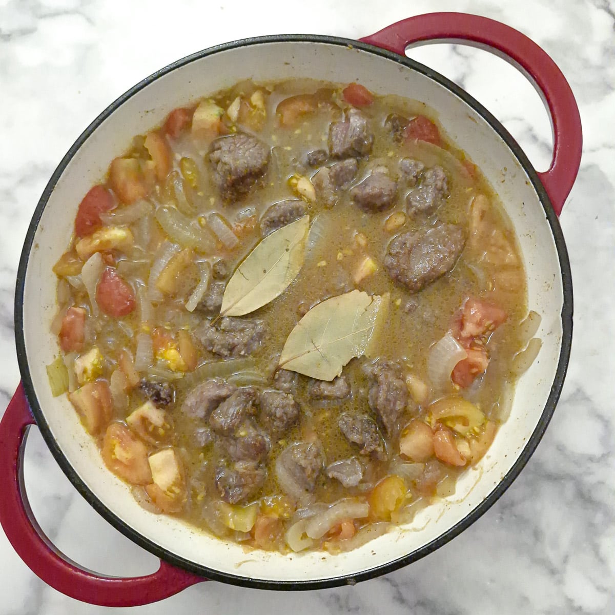 Step 4, browned meat returned to the pan and covered with stock. There are 2 bay leaves floating on top.