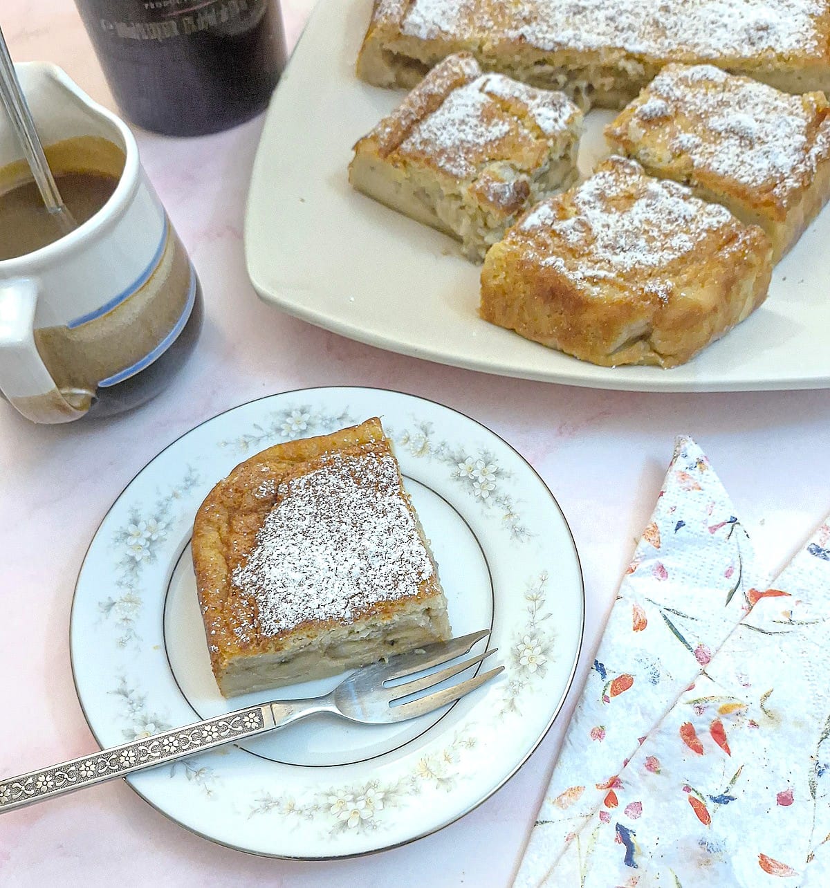 Overhead shot of a slice of caramelised banana magic cake on a small plate.  There are slices of cake on a plate in the background along with a jug of caramel sauce.