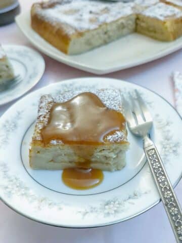 A slice of caramelised banana magic cake on a blue patterned plate, drizzled with caramel sauce.