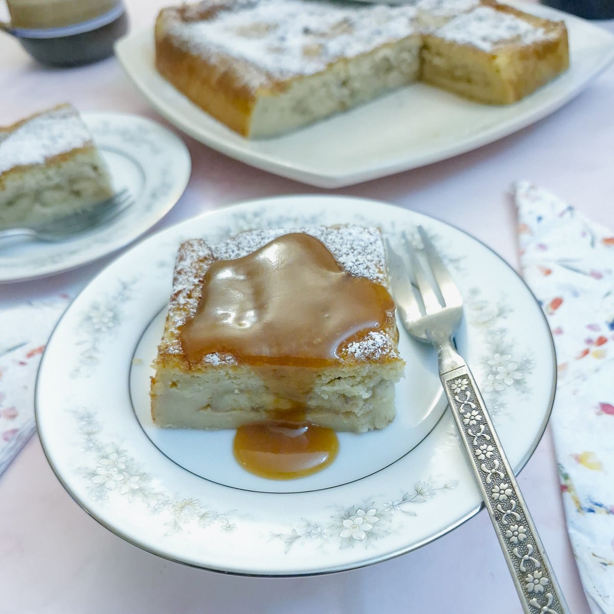 A slice of Baileys caramelised banana magic cake on a blue patterned plate, drizzled with caramel sauce.
