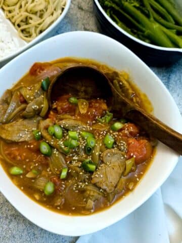 A white dish of Cantonese-style pork and tomao stir-fry with a large wooden serving spoon.
