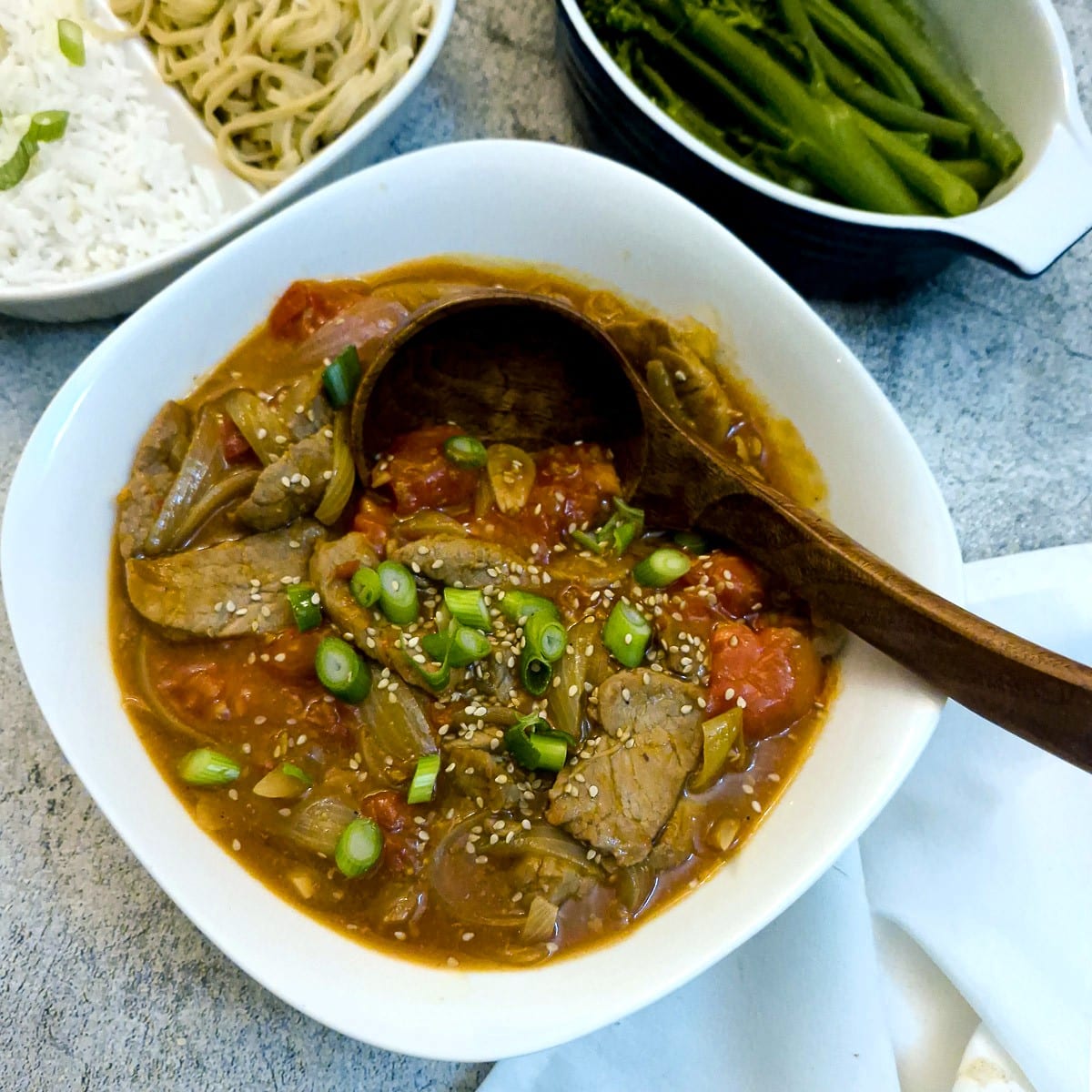 A white dish of Cantonese-style pork and tomao stir-fry with a large wooden serving spoon.