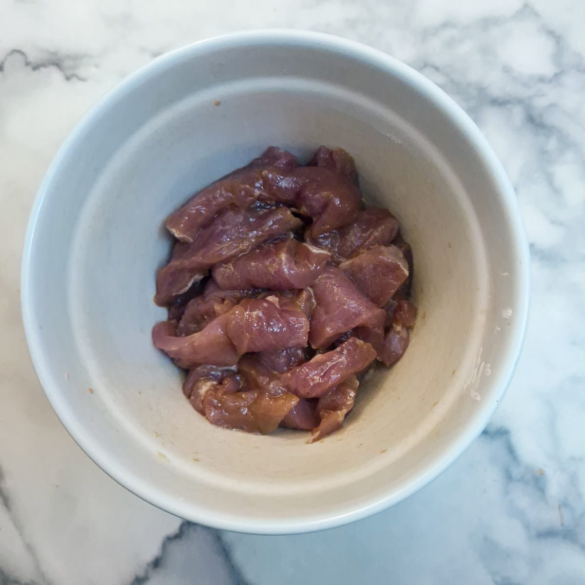 Slices of pork marinating in a small bowl.