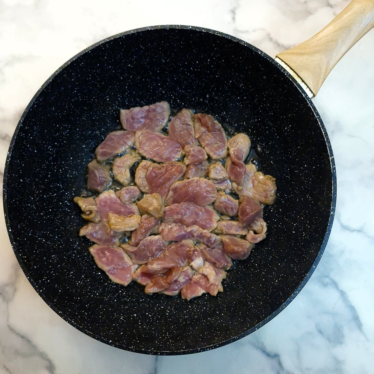 Slices of pork being browned in a wok.