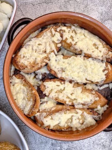 A brown cassrole dish of French onion beef stew topped with slices of cheesy bread.