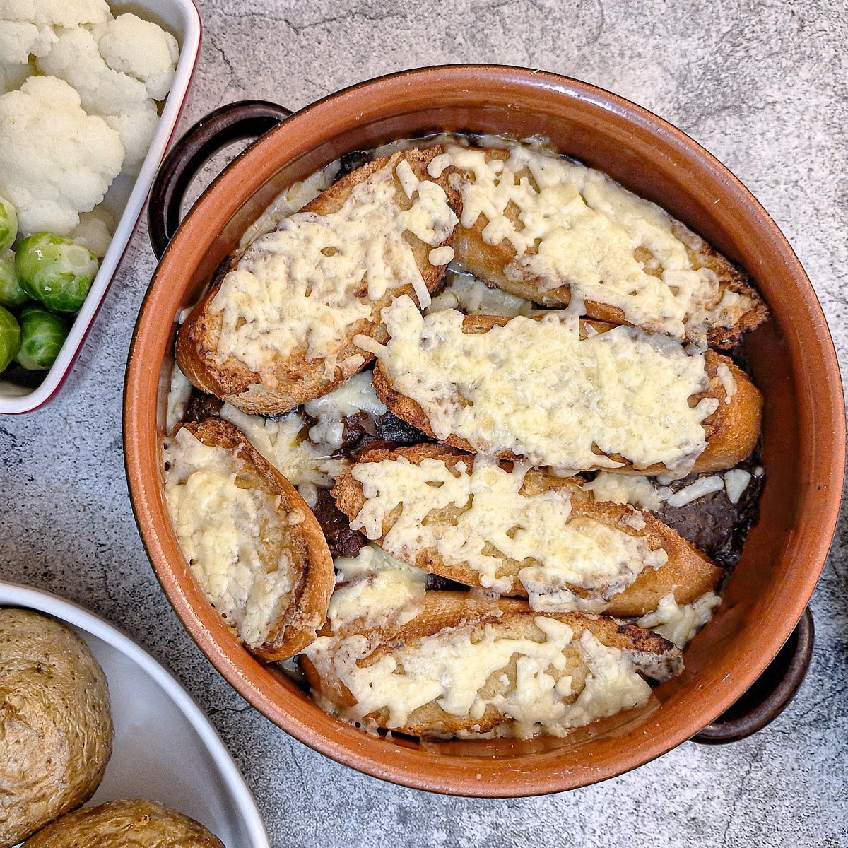 A brown cassrole dish of French onion beef stew topped with slices of cheesy bread.