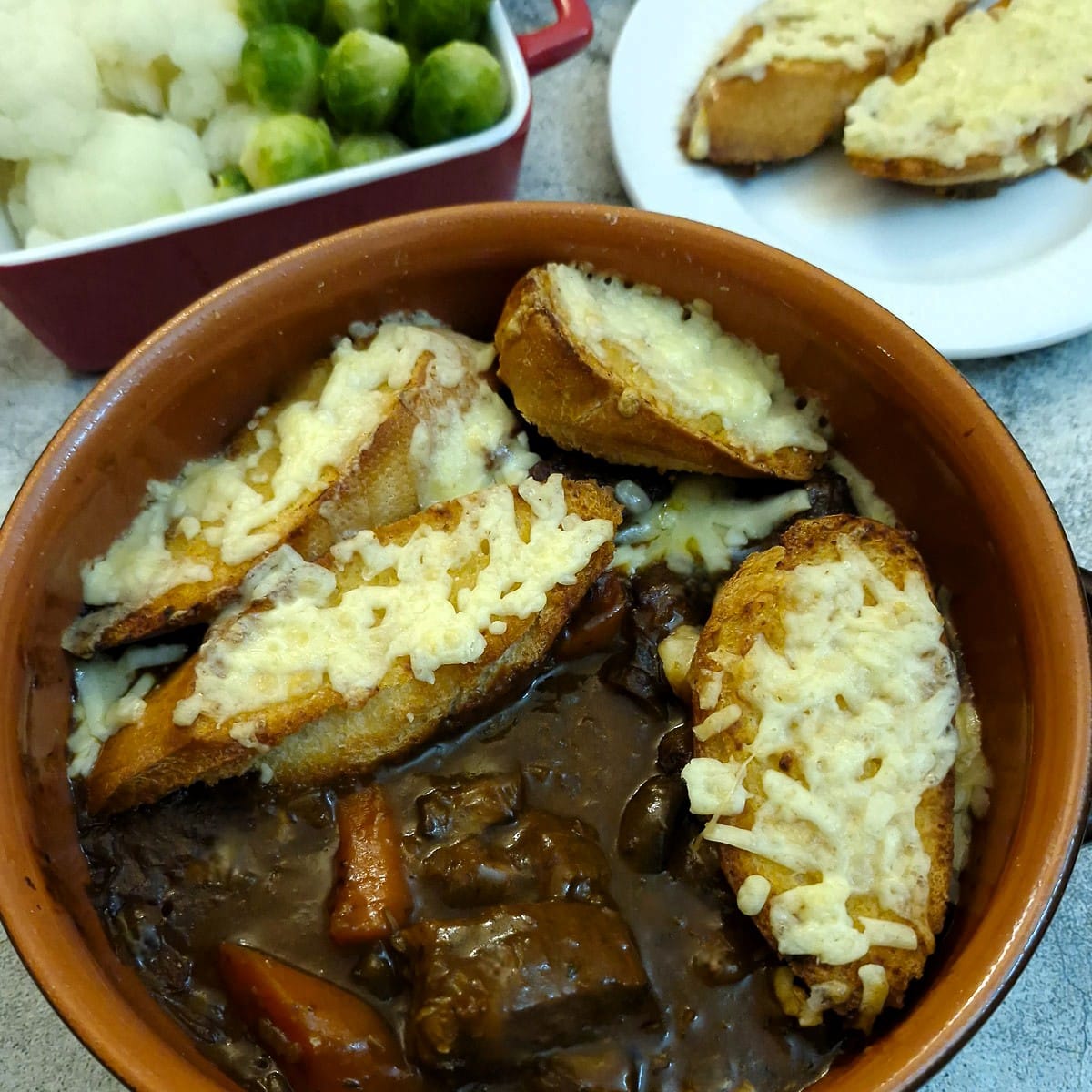 French onion beef stew topped with cheesy bread with a few slices of bread removed to show the meat and gravy beneath.