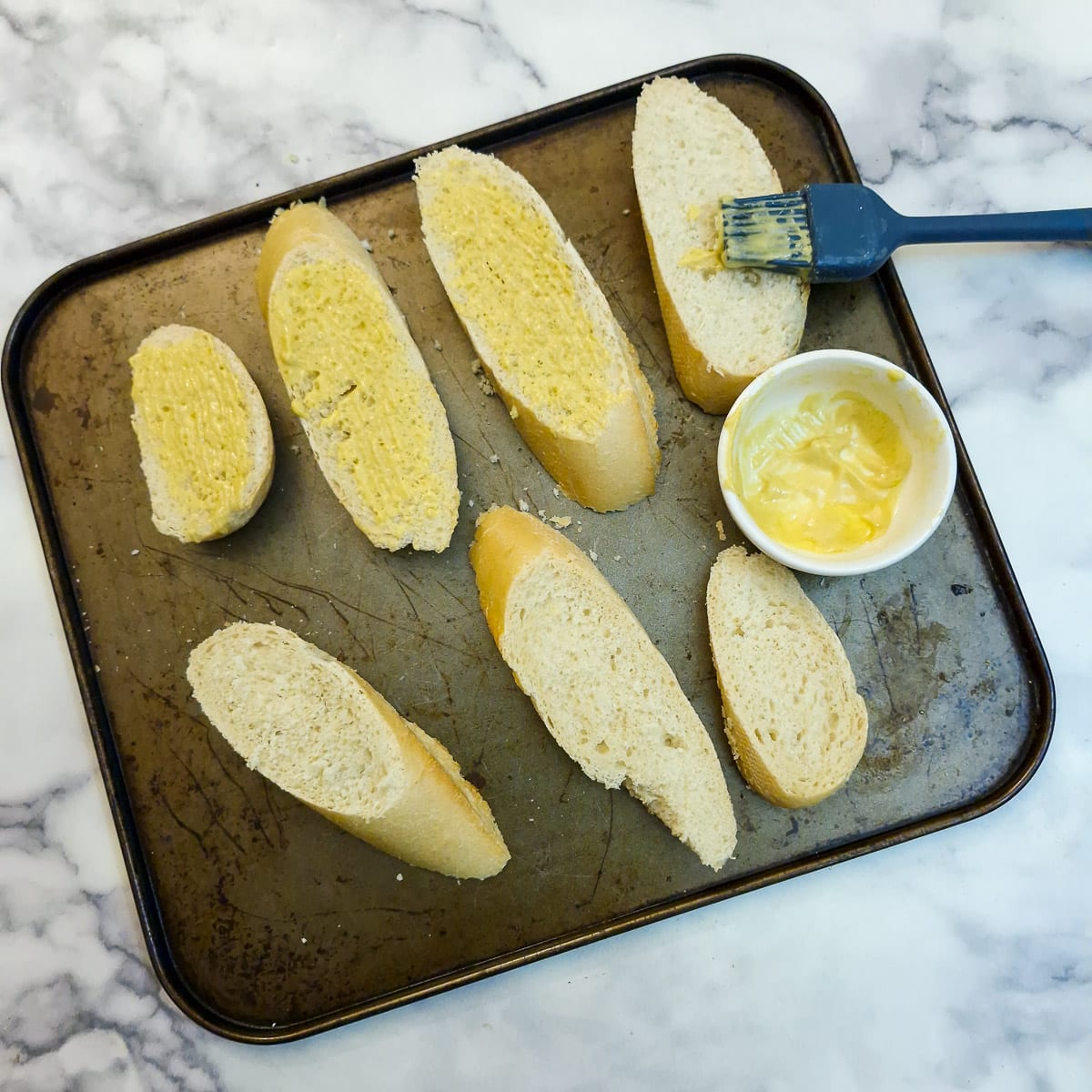 Slices of baguette being brushed with a mixture of olive oil and mustard.