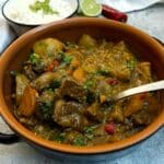 A brown dish of Thai-style Massaman curry with a large serving spoon lifting the beef from the dish.