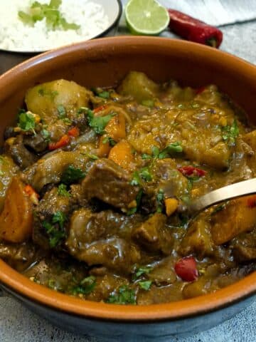 A brown dish of Thai-style Massaman curry with a large serving spoon lifting the beef from the dish.
