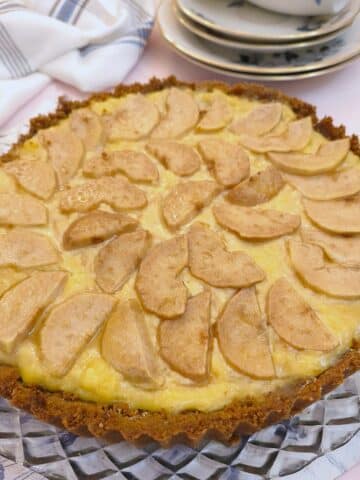 A round baked pear and ginger tart on a glass plate. There are slices of pears arranged on top of the custard filling.