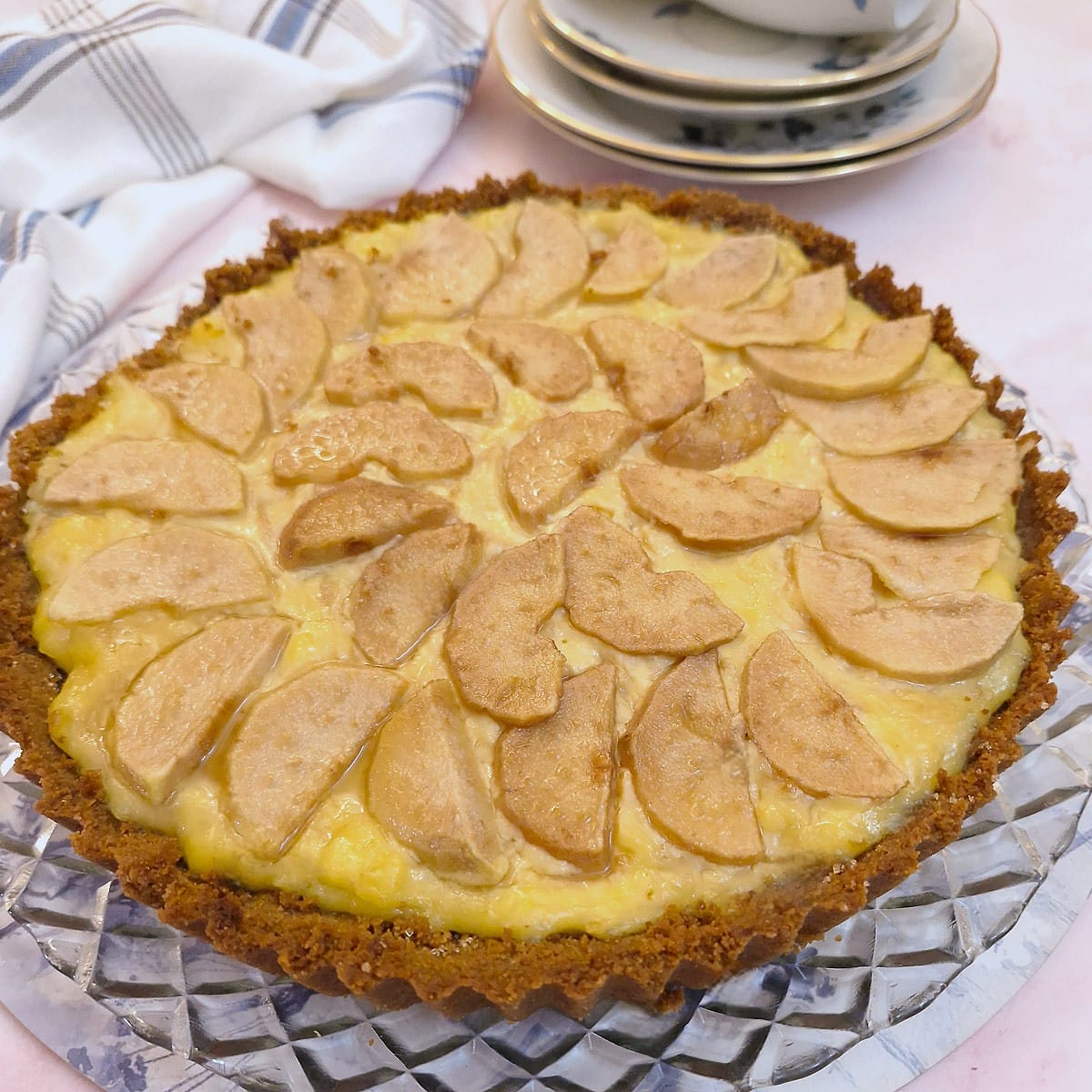 A round baked pear and ginger tart on a glass plate. There are slices of pears arranged on top of the custard filling.