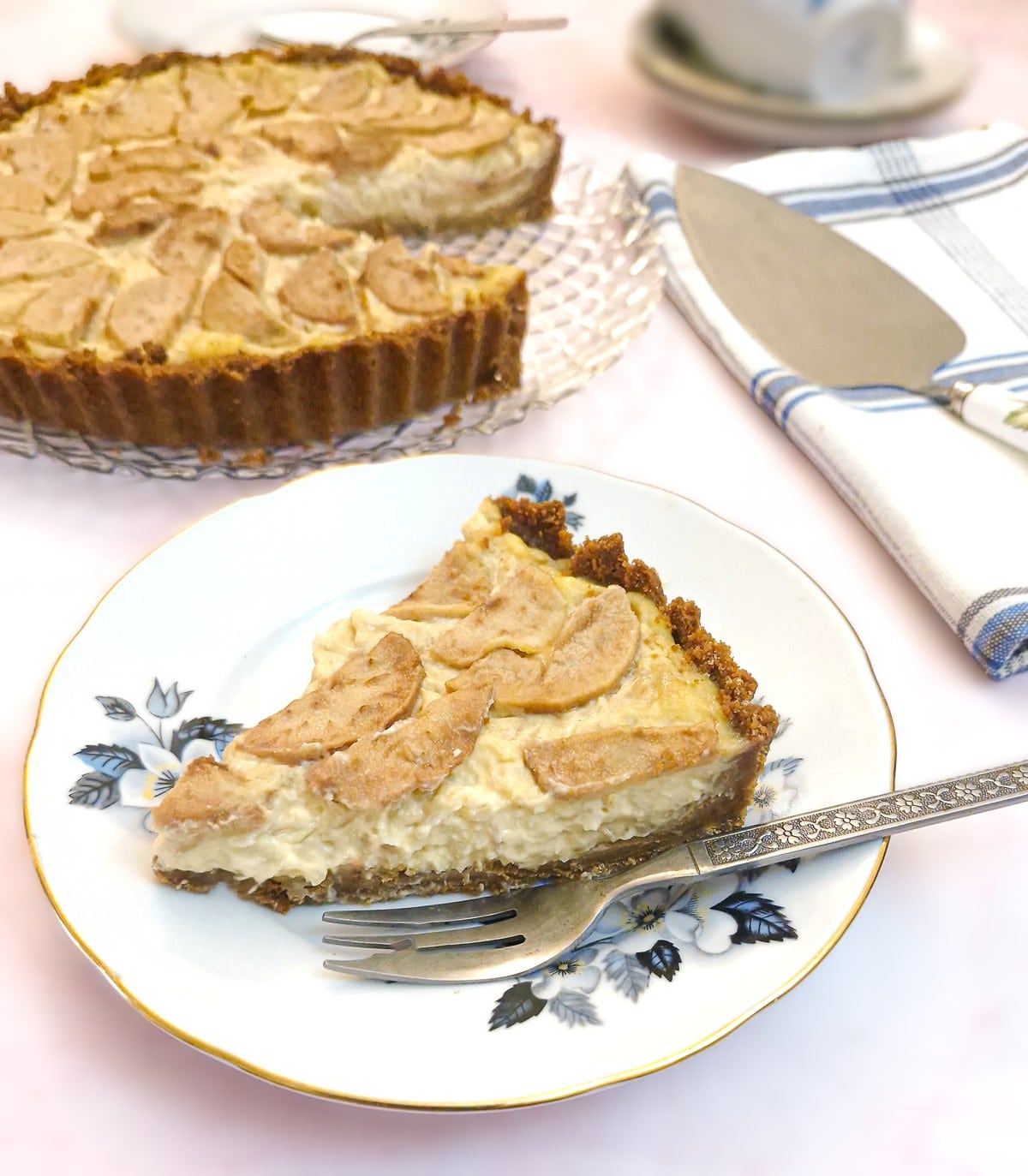Close up of a slice of pear and ginger tart on a blue flowered plate. The larger tart is in the background.