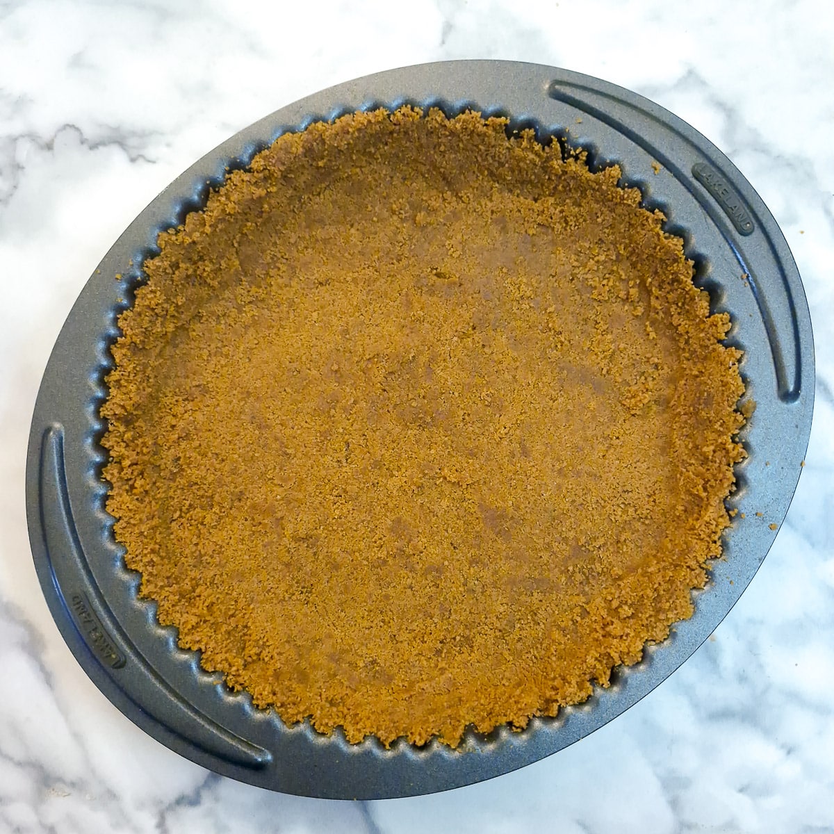 Step 3 - ginger biscuit crumbs pressed into the base and sides of a round baking dish.