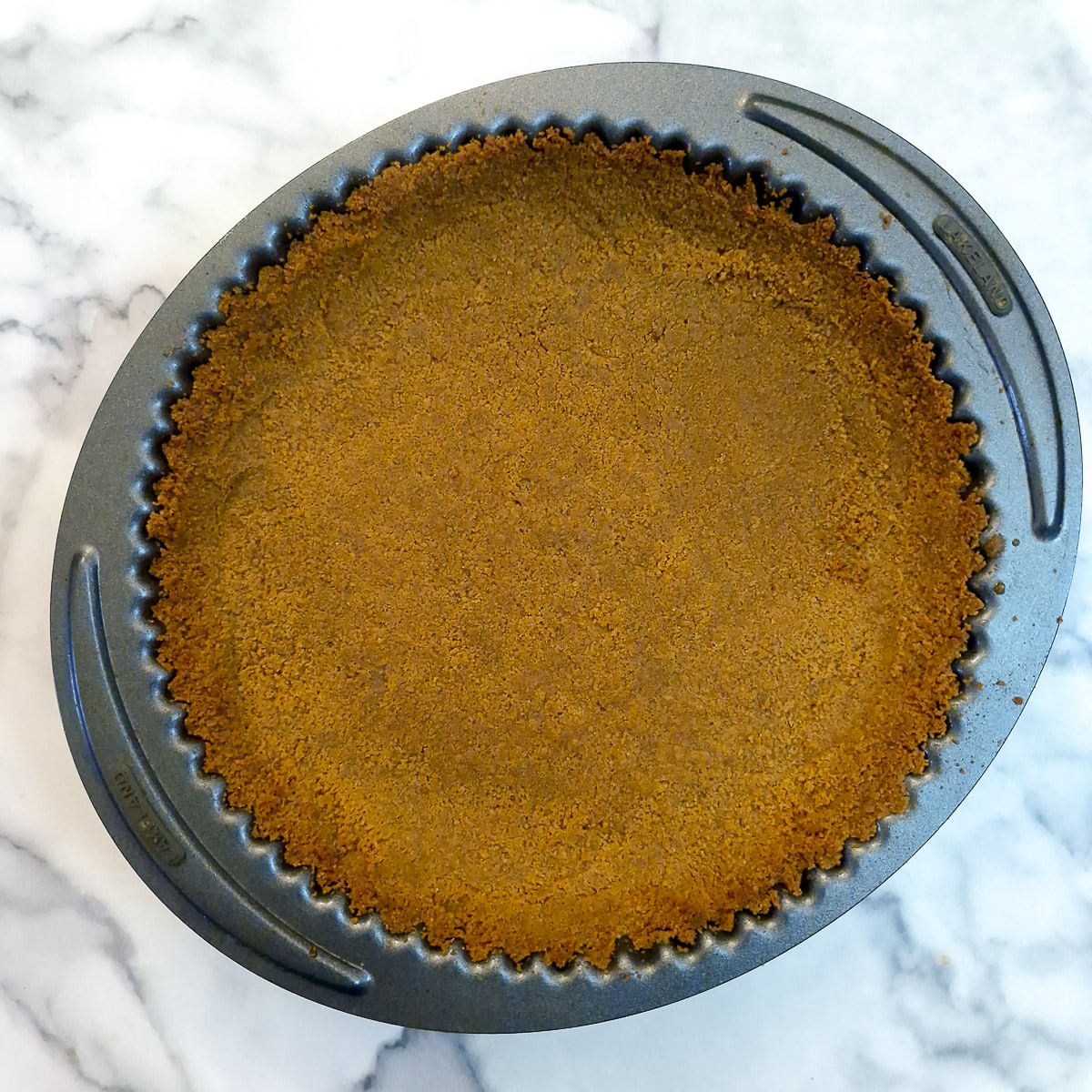 Step 4 - a baked ginger biscuit pie crust in a round baking tin.