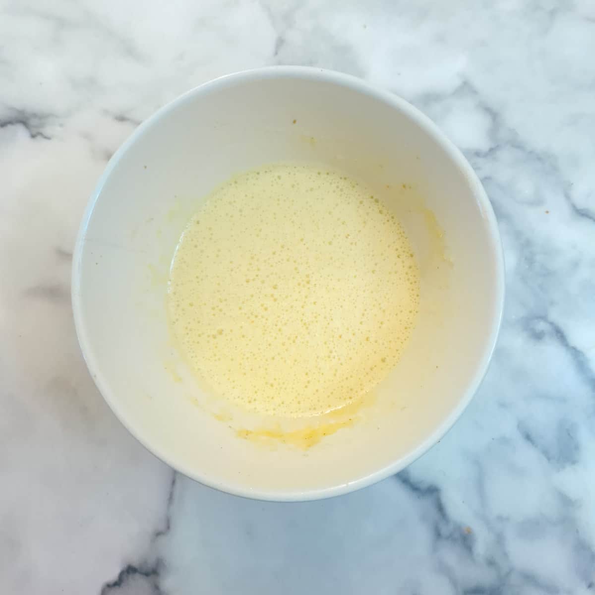 Step , eggs, sugar and flavourings combined in a smalll white mixing bowl.