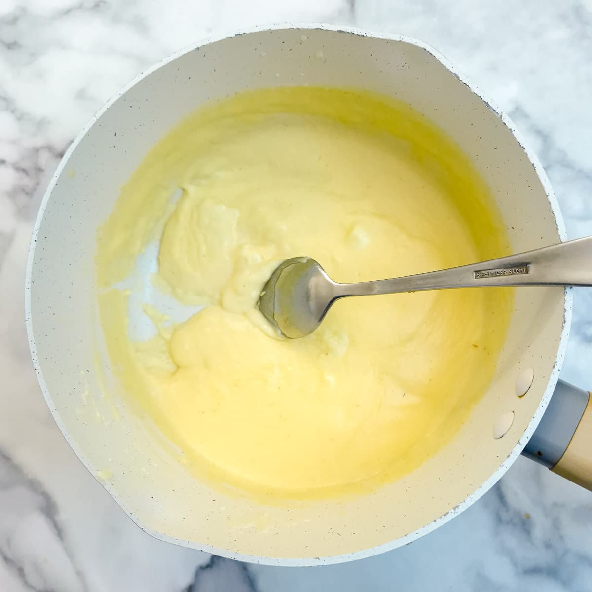 Step 7, thickened custard in a small saucepan. There is a spoon drawing a trail through the custard.