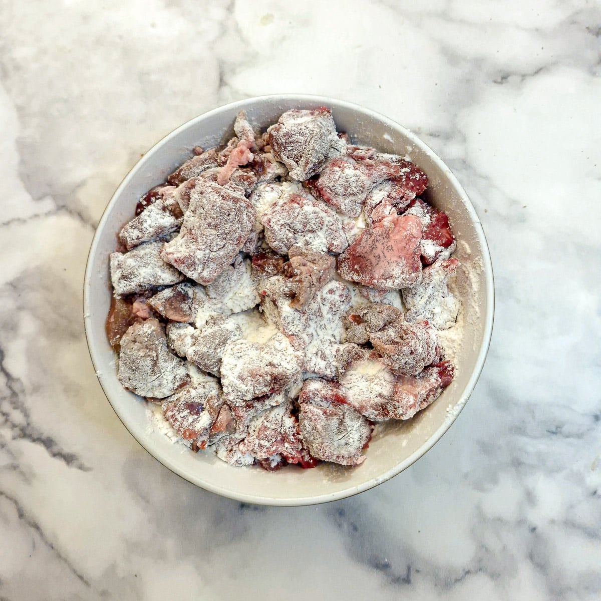 Step 1, pieces of steak and kidney coated with seasoned flour in a small bowl.