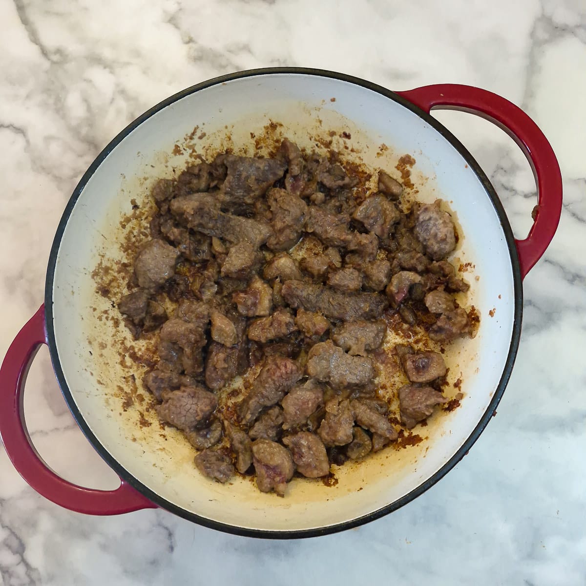 Step 2, flour coated steak and kidney being browned in a cast-iron pan.