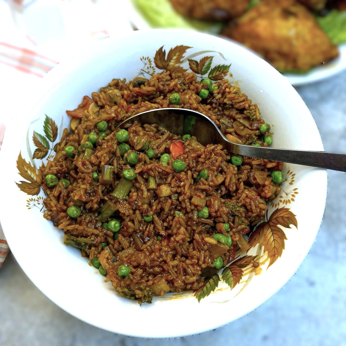 Overhead shot of sweet chilli vegetable rice in an autumn leaf patterned serving dish with a large serving spoon.