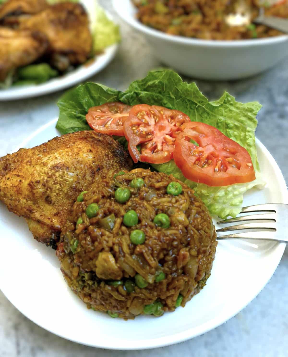 A mound of sweet chilli vegetable rice on a plate with a peri peri chicken thigh, lettuce and sliced tomato.