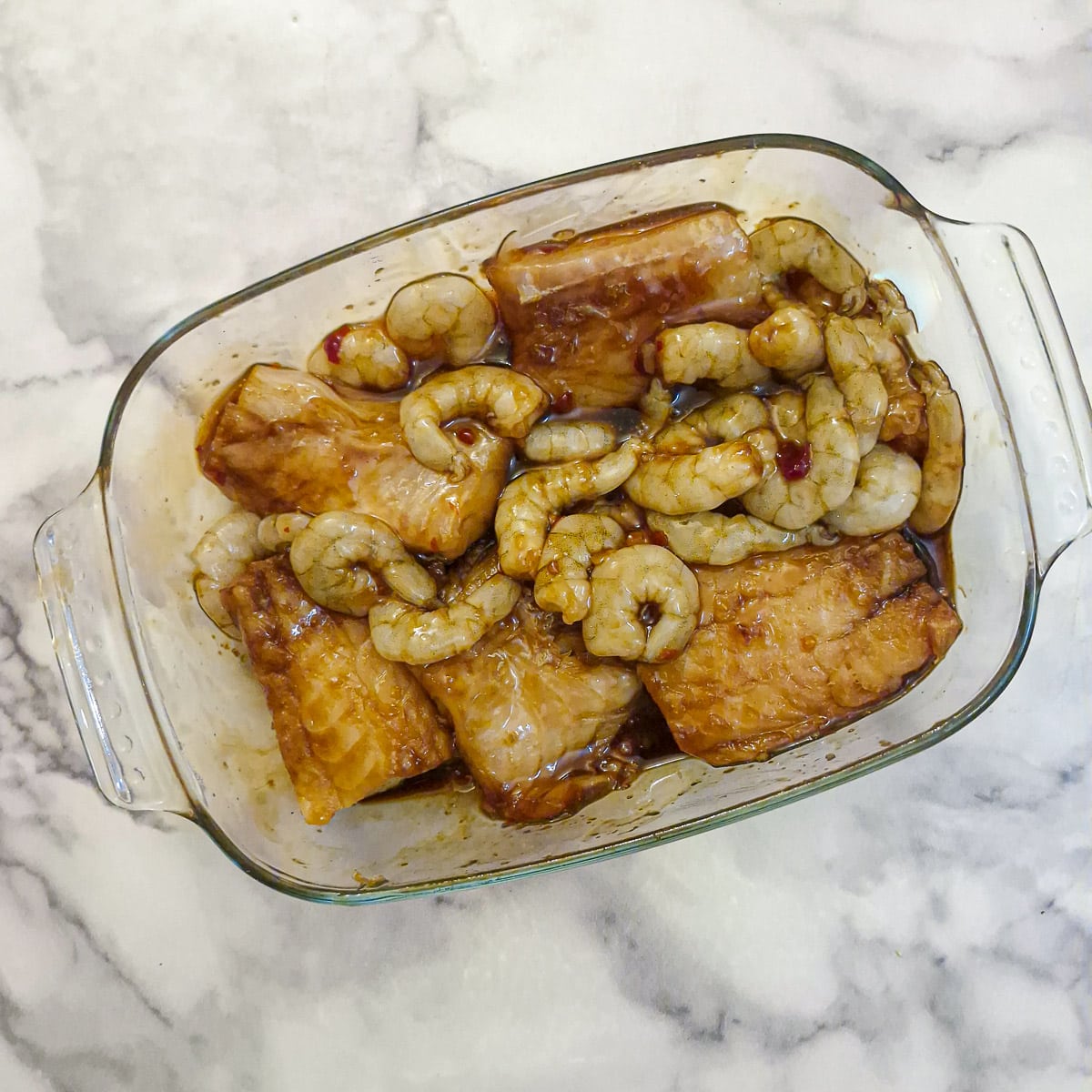 Fish fillets and prawns marinating in an oblong glass dish.