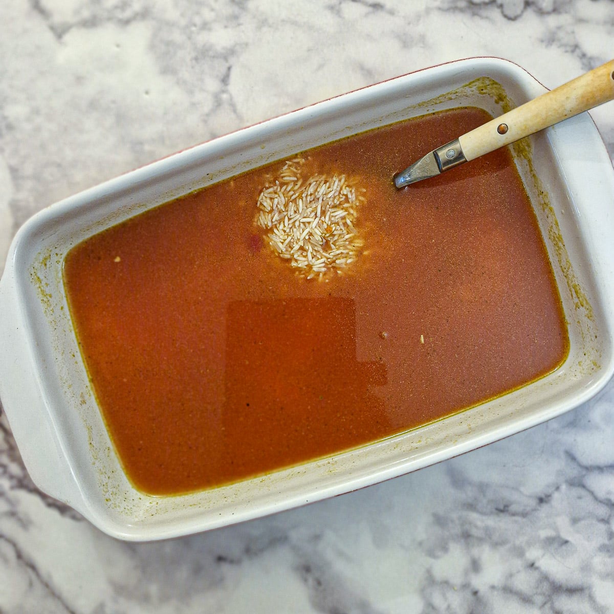 Rice and stock in an oblong white ceramic baking dish.