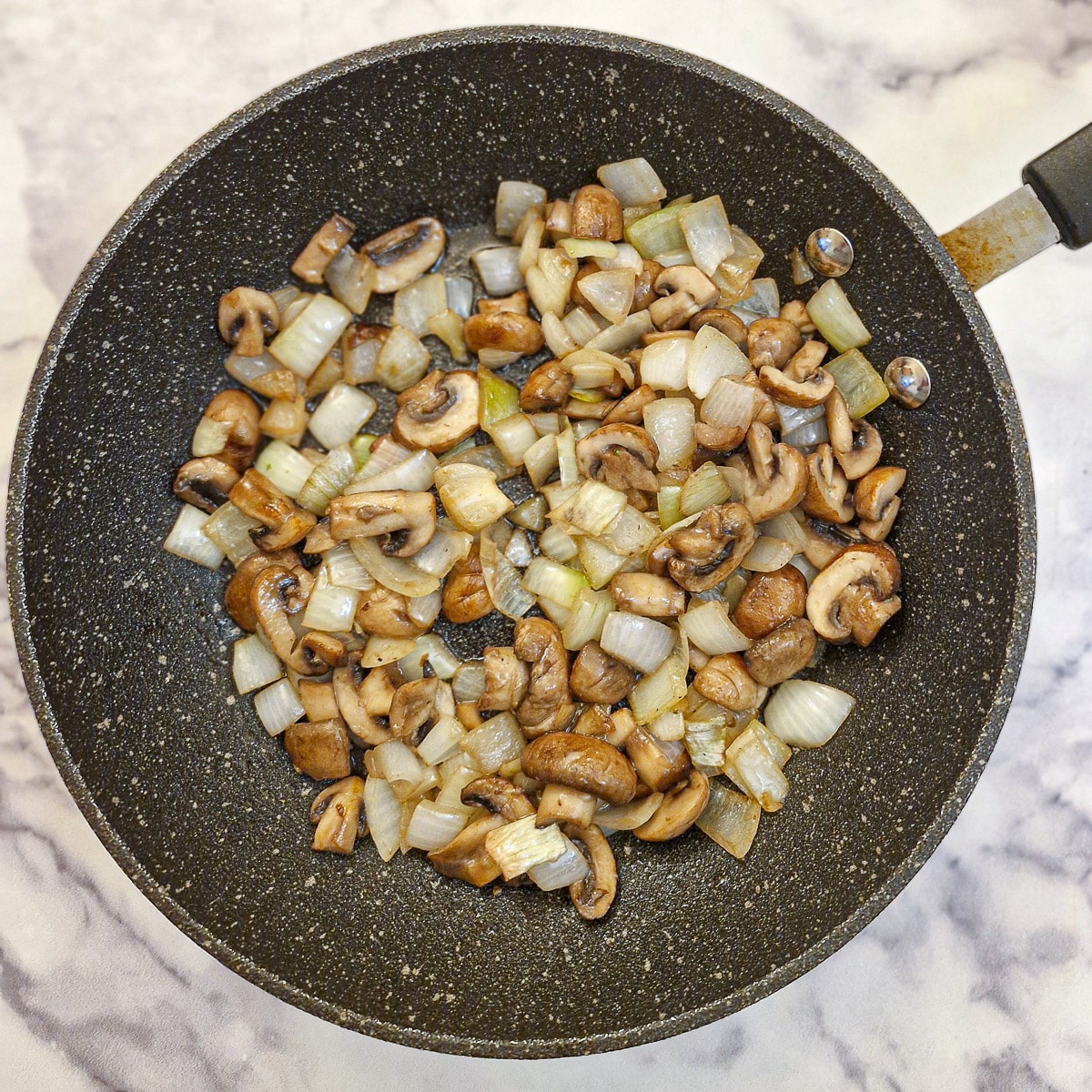 Mushrooms, bell peppers and onions softening in a black frying pan.