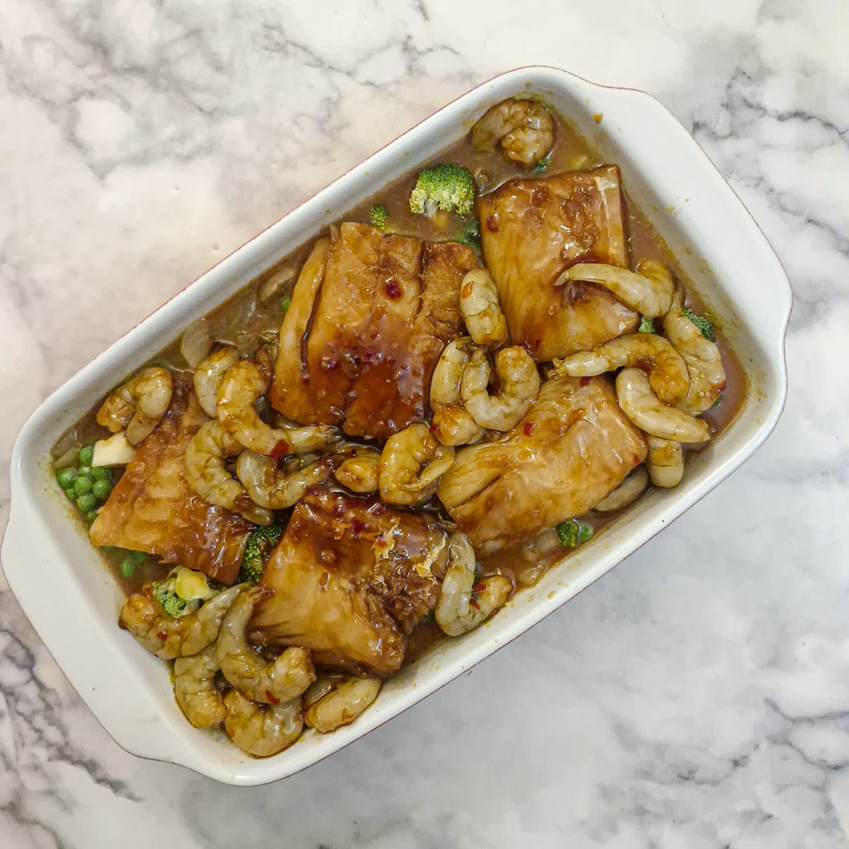 Marinated pieces of fish and prawns nestled into the stock in a the white ceramic baking dish.