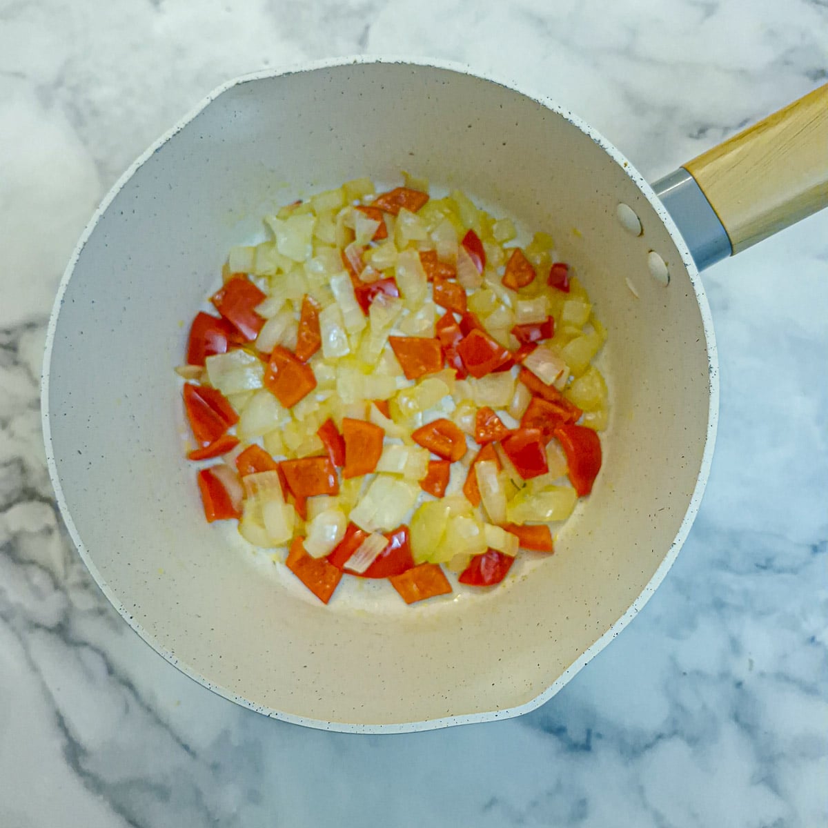 Onions and red bell peppers softening in a saucepan.