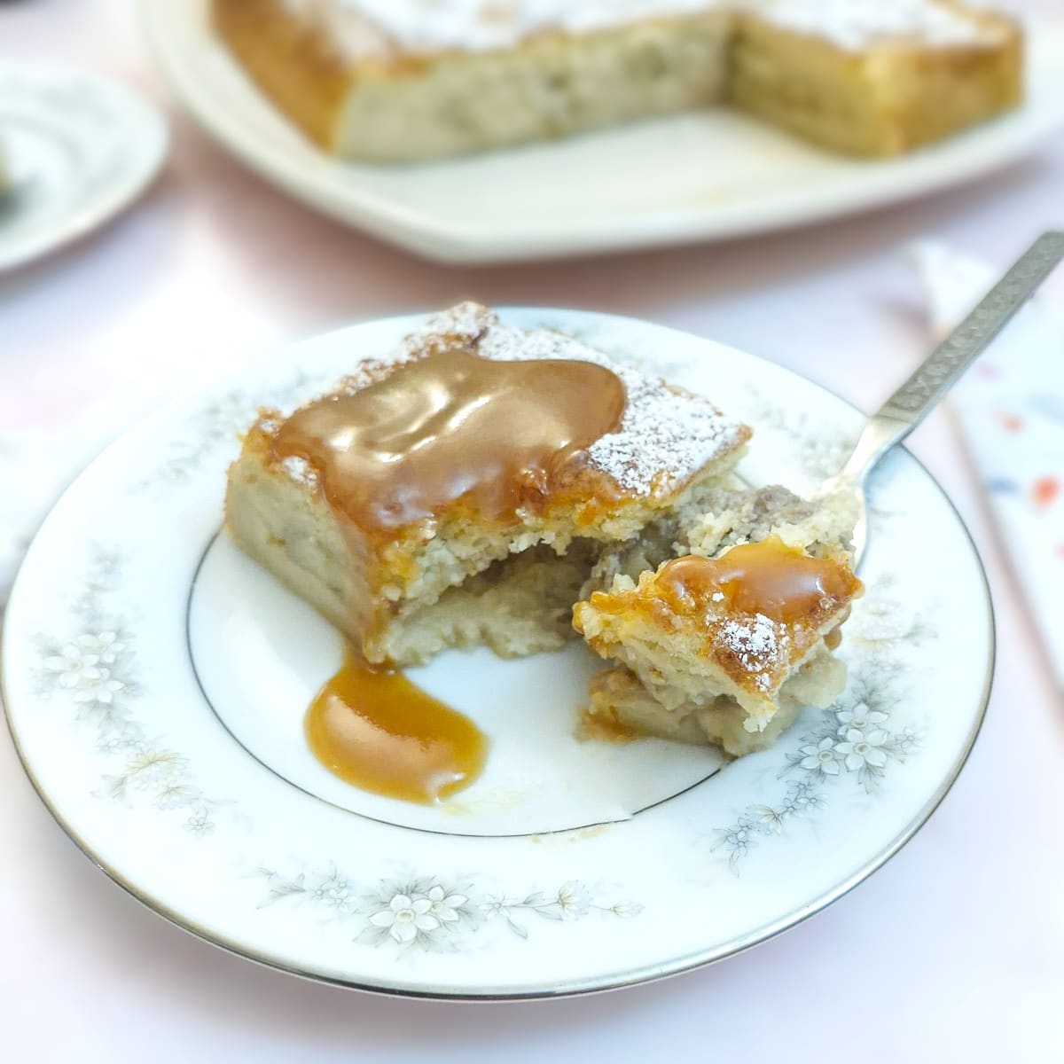 A slice of caramelised banana magic cake on a plate, with caramel sauce.  A cake fork is being used to scoop a mouthful of cake.
