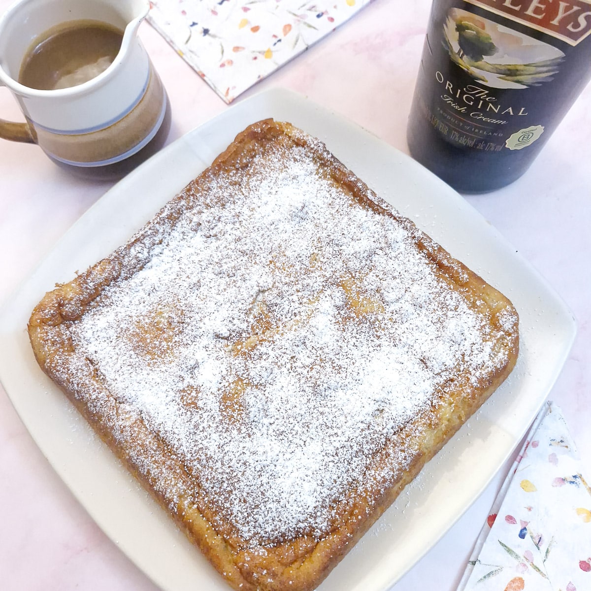 A square Baileys banana magic cakke on a squar white plate, sprinkled with icing sugar.