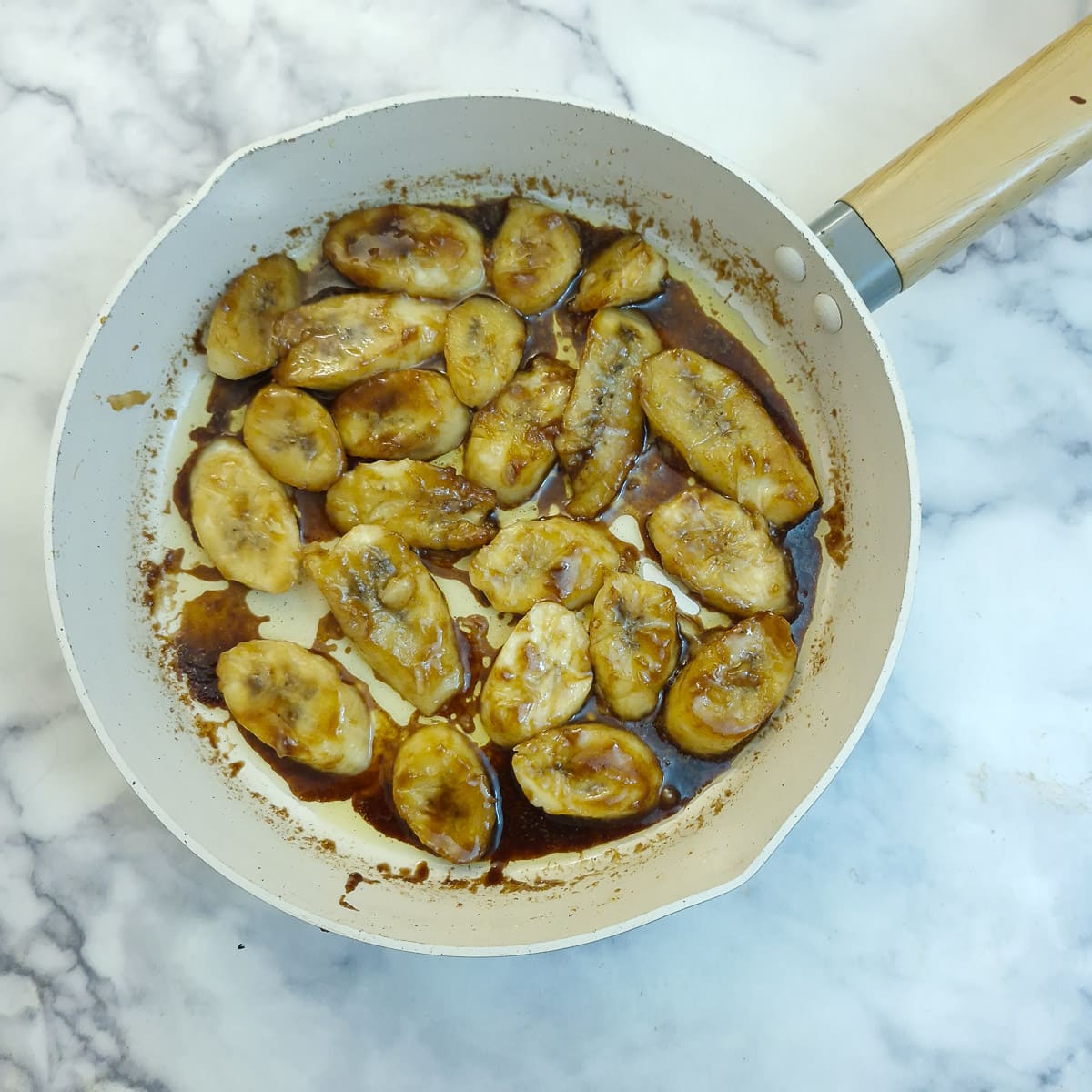 Sliced bananas caramelising in a sauepan with butter and brown sugar.