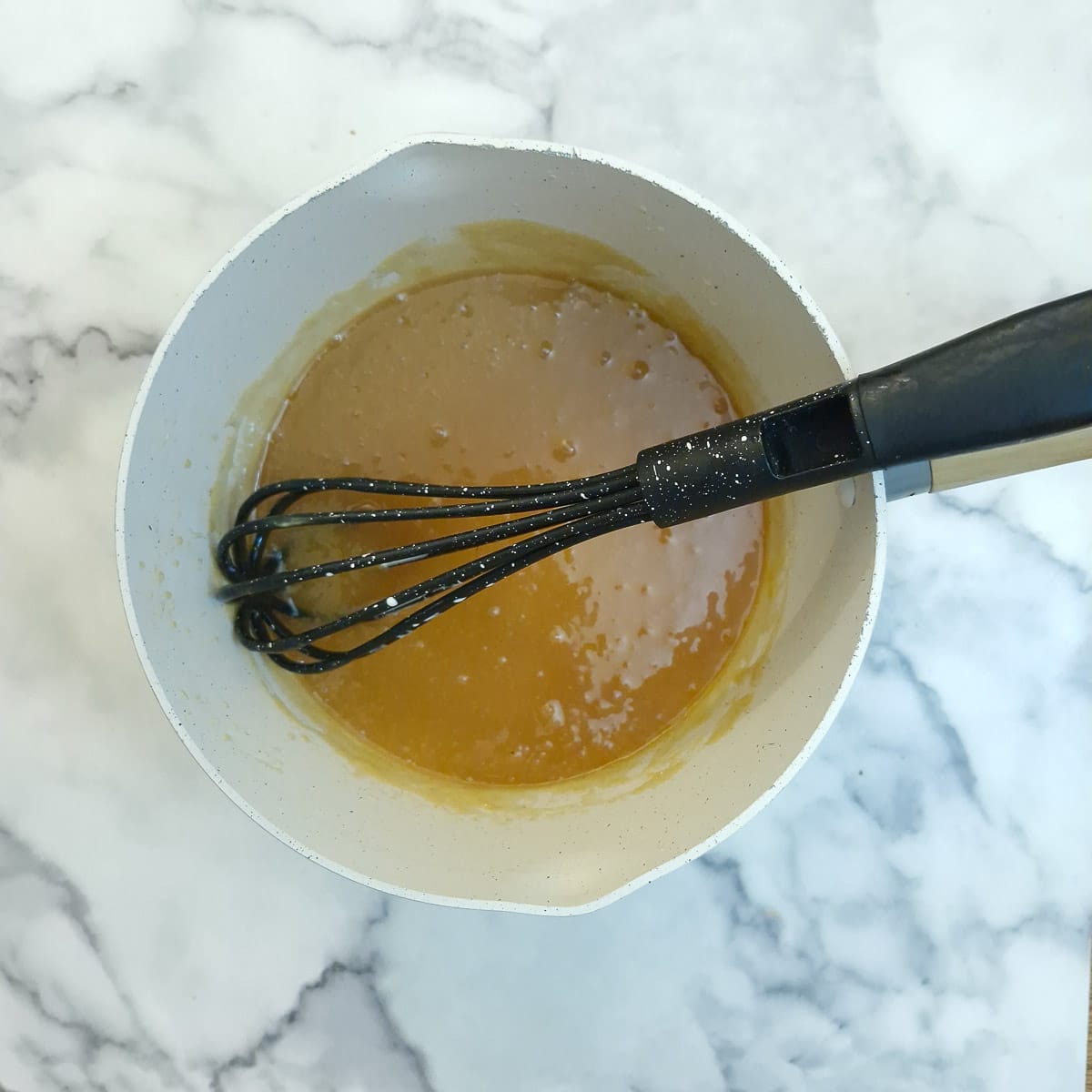 Cream stirred into the caramel sauce and cooked for 2 to 3 minutes to allow it to thicken.  There is a balloon whisk in the pan.