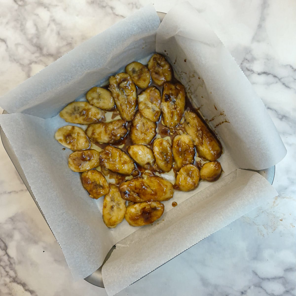 Caramelised banana slices arranged in a single layer in a baking dish lined with baking parchment.