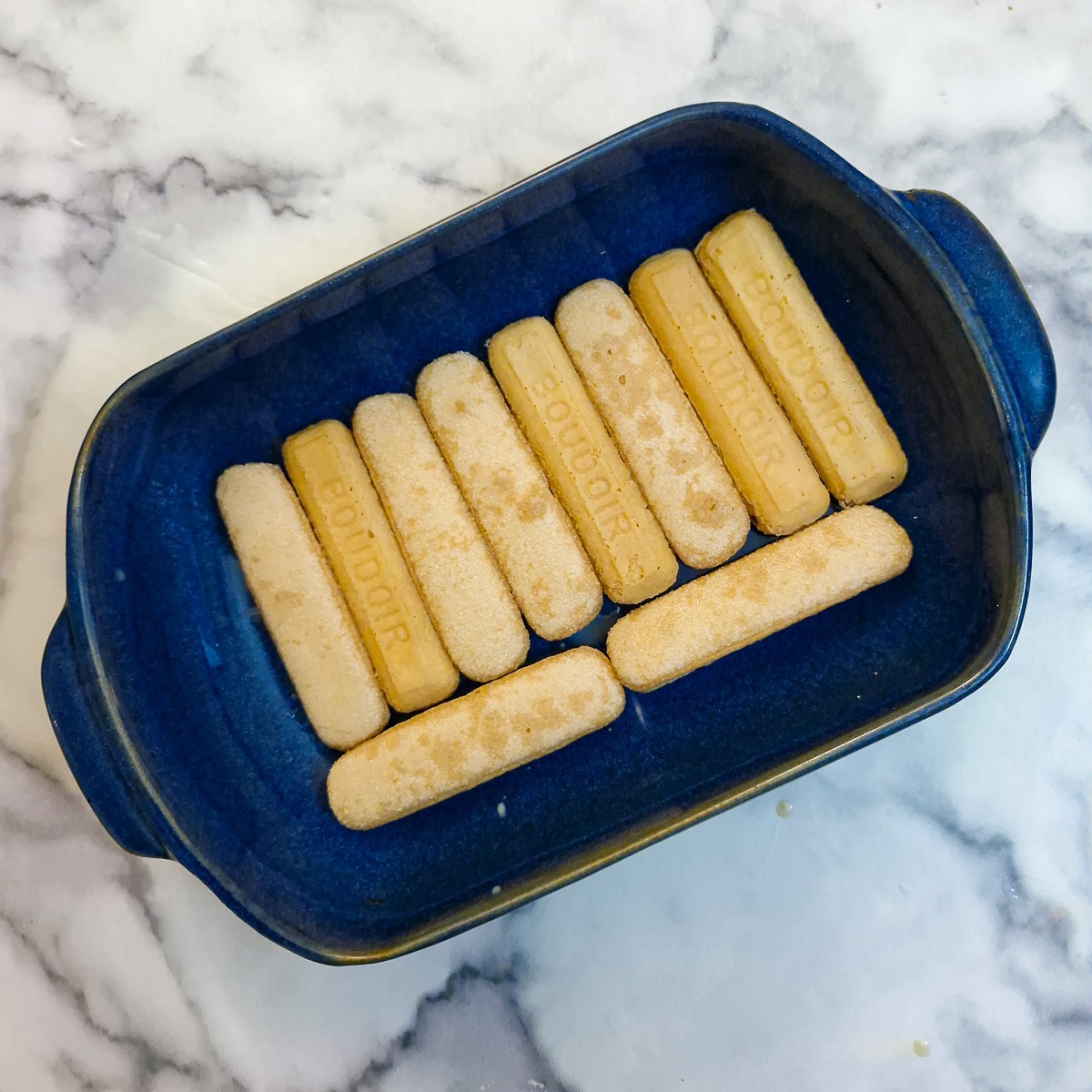 Sponge finger biscuts which have been dipped in Baileys, arranged in a blue dish.