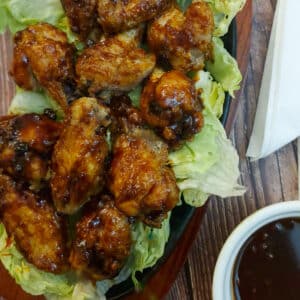 A pile of gochujang chicken wings on bed of lettuce leaves. There is a small dish of extra sauce in the foreground.